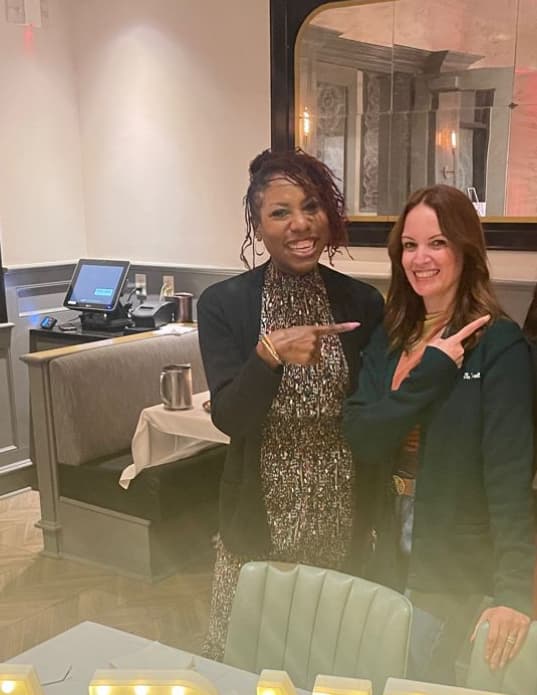 Dr. Natalie Edwards-Hudson posing playfully with a colleague at a restaurant celebration