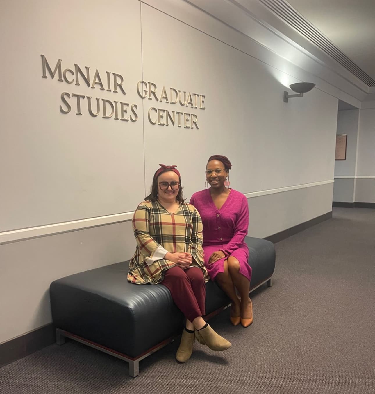 Dr. Natalie Edwards-Hudson seated with a colleague beneath the McNair Graduate Studies Center sign
