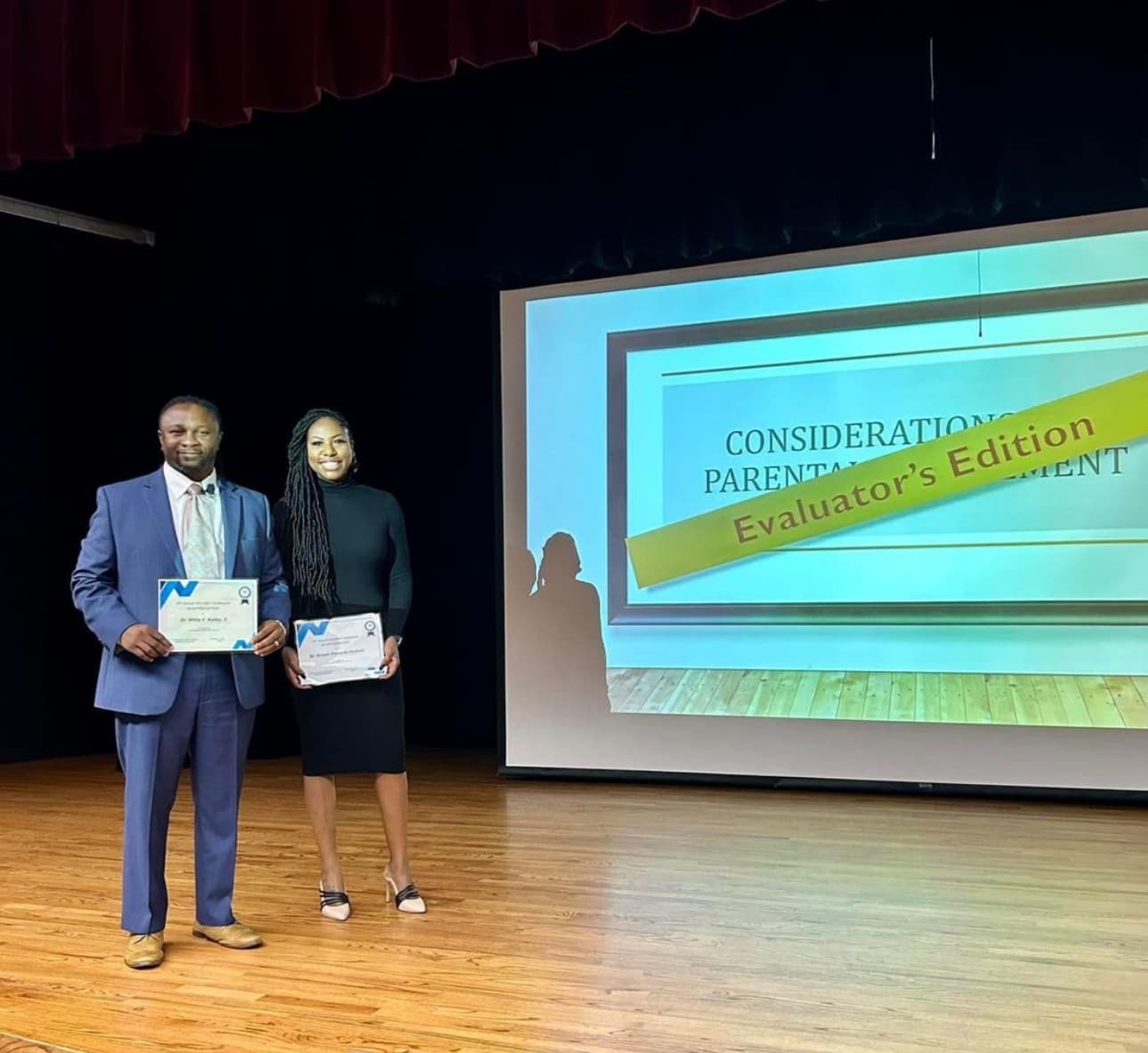 Dr. Natalie Edwards-Hudson on stage receiving a certificate alongside a colleague at an awards presentation