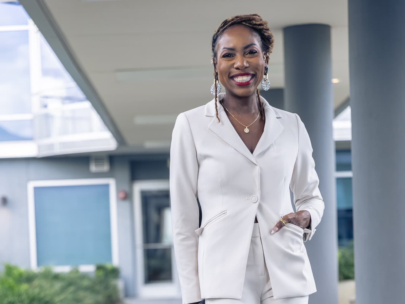 Dr. Natalie Edwards-Hudson, smiling and wearing a cream blazer suit, walking beneath a covered outdoor walkway